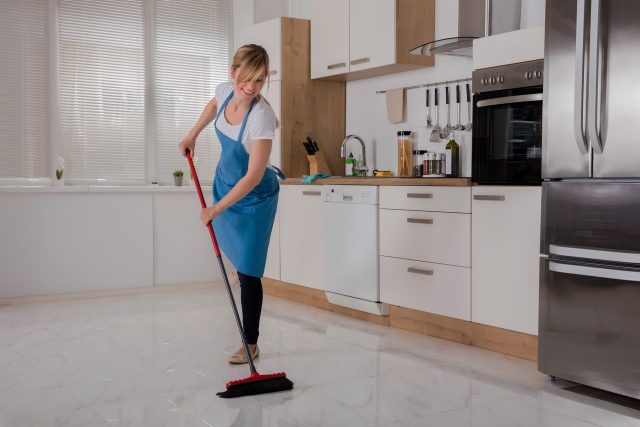 mulher a limpar a cozinha com uma vassoura